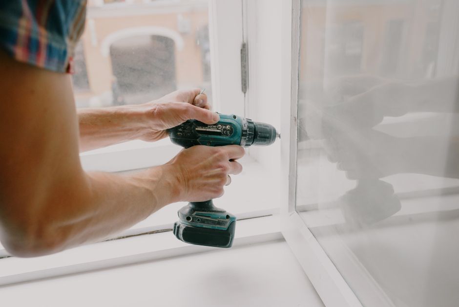 Hands fixing a window frame with a screwdriver during a renovation.